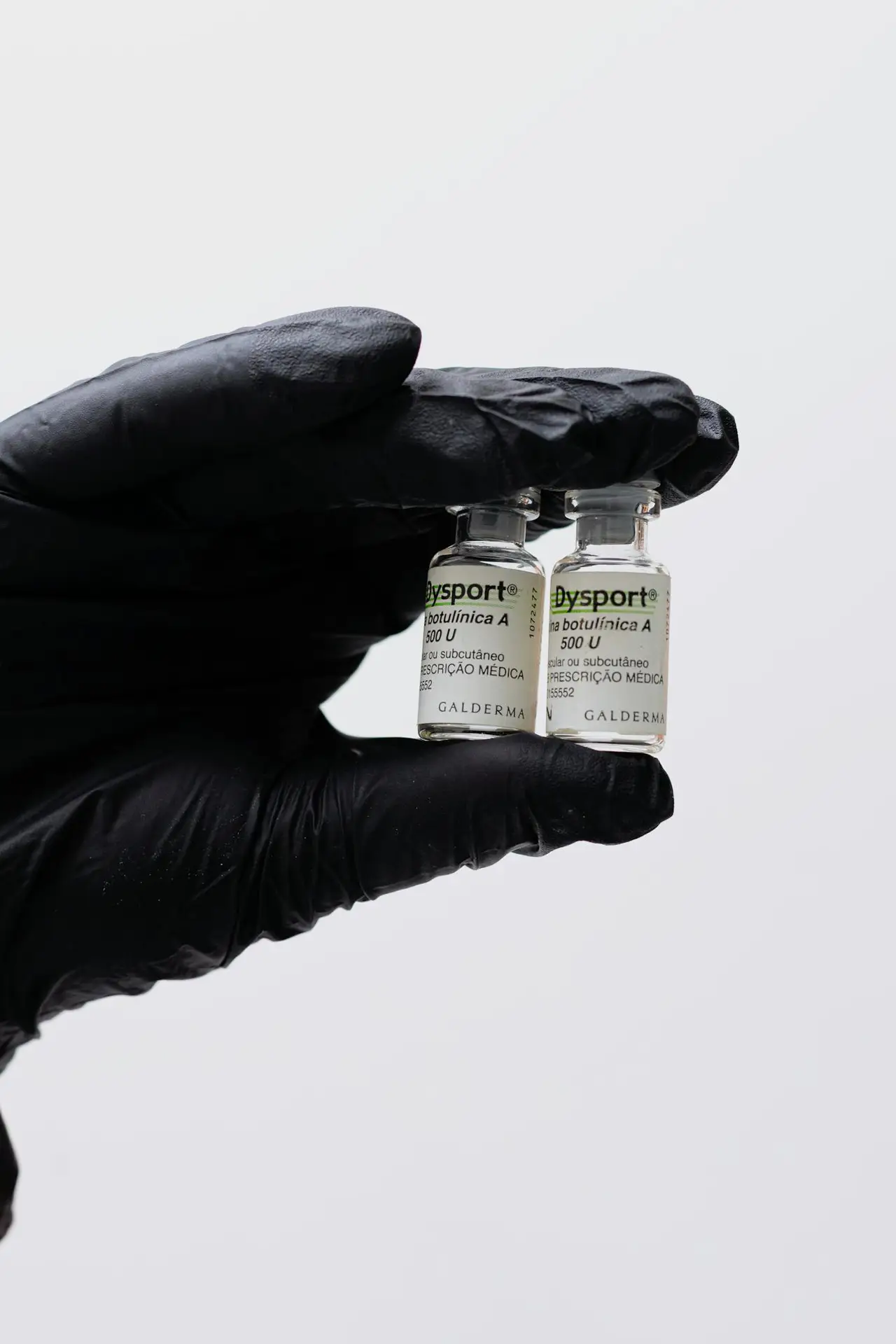 Close-up image of a gloved hand holding two Dysport botulinum toxin vials.